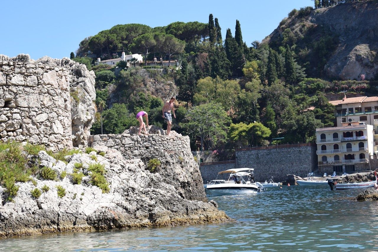 Clear blue water and moored boats in the sheltered bay of Mazzaro below the Taormina hillside