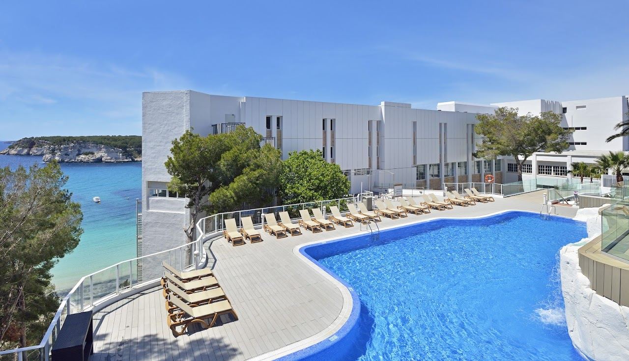 Beachfront and pool terrace of a resort hotel above the sand at Cala Galdana in Menorca