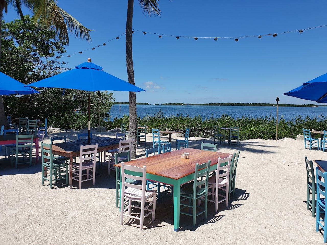 White Adirondack chairs on the palm lined bayside sand at Morada Bay Beach Cafe in Islamorada