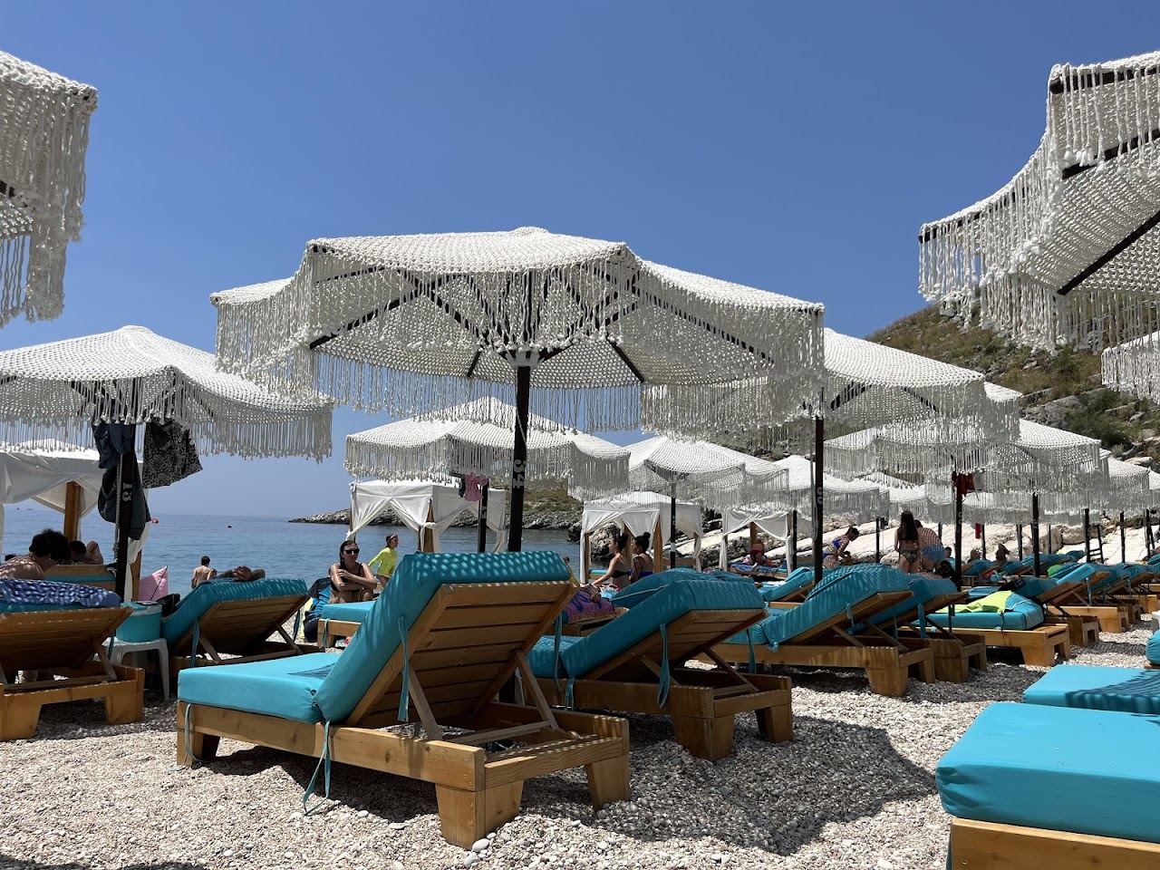 Sunbeds and umbrellas of Mumbas Beach Club on the turquoise water of Llamani cove south of Himara, Albania