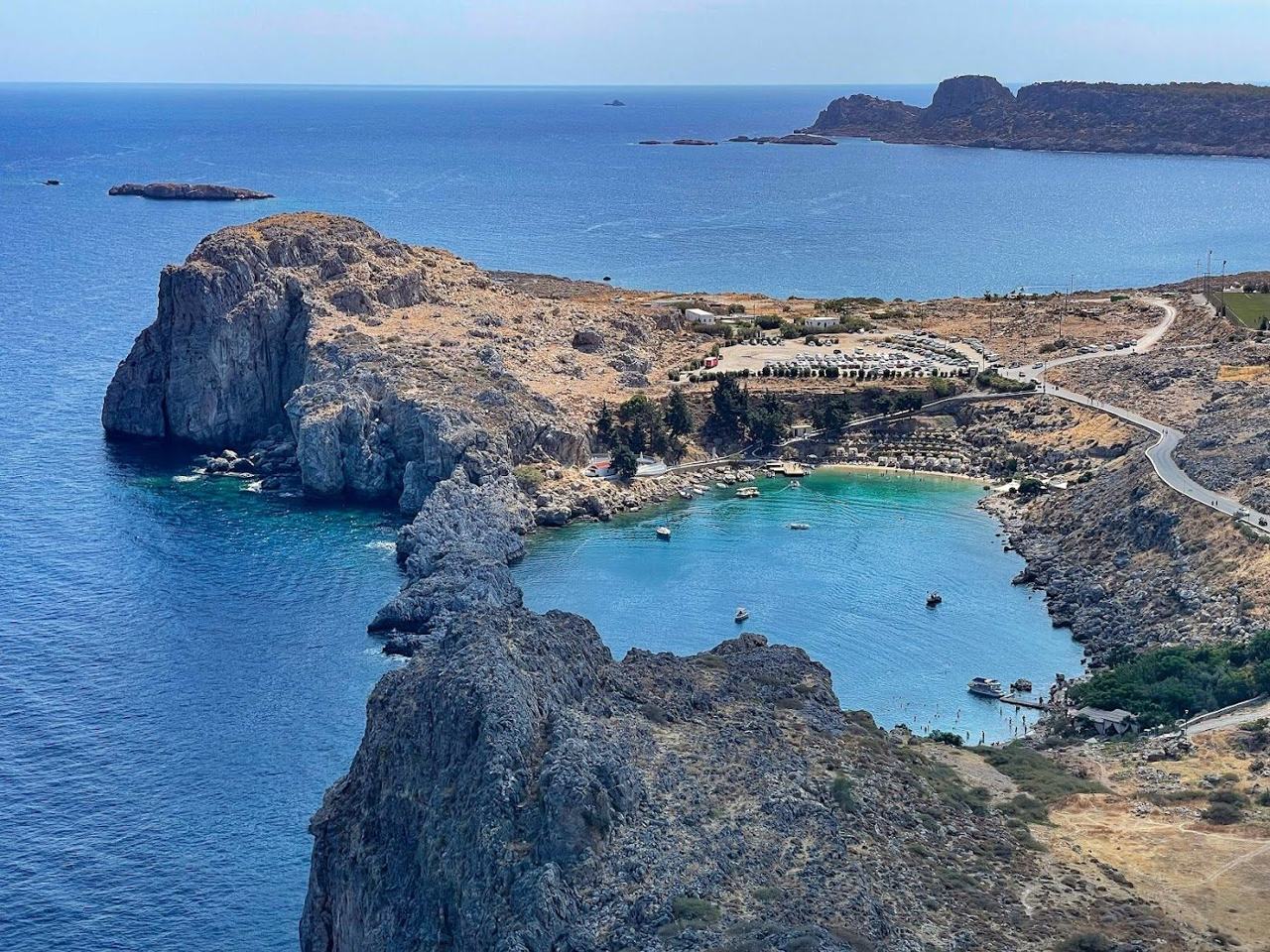 A sheltered blue bay below a clifftop village on a quiet stretch of Rhodes