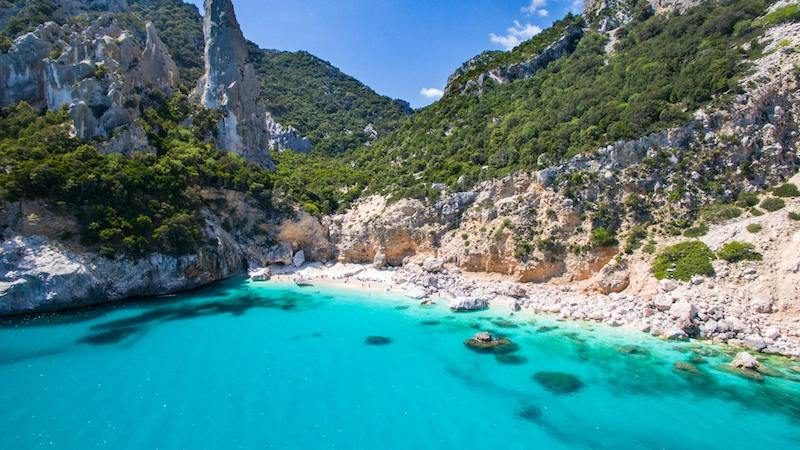 A wild cove of pale pebbles and clear water reached only on foot, empty in high summer