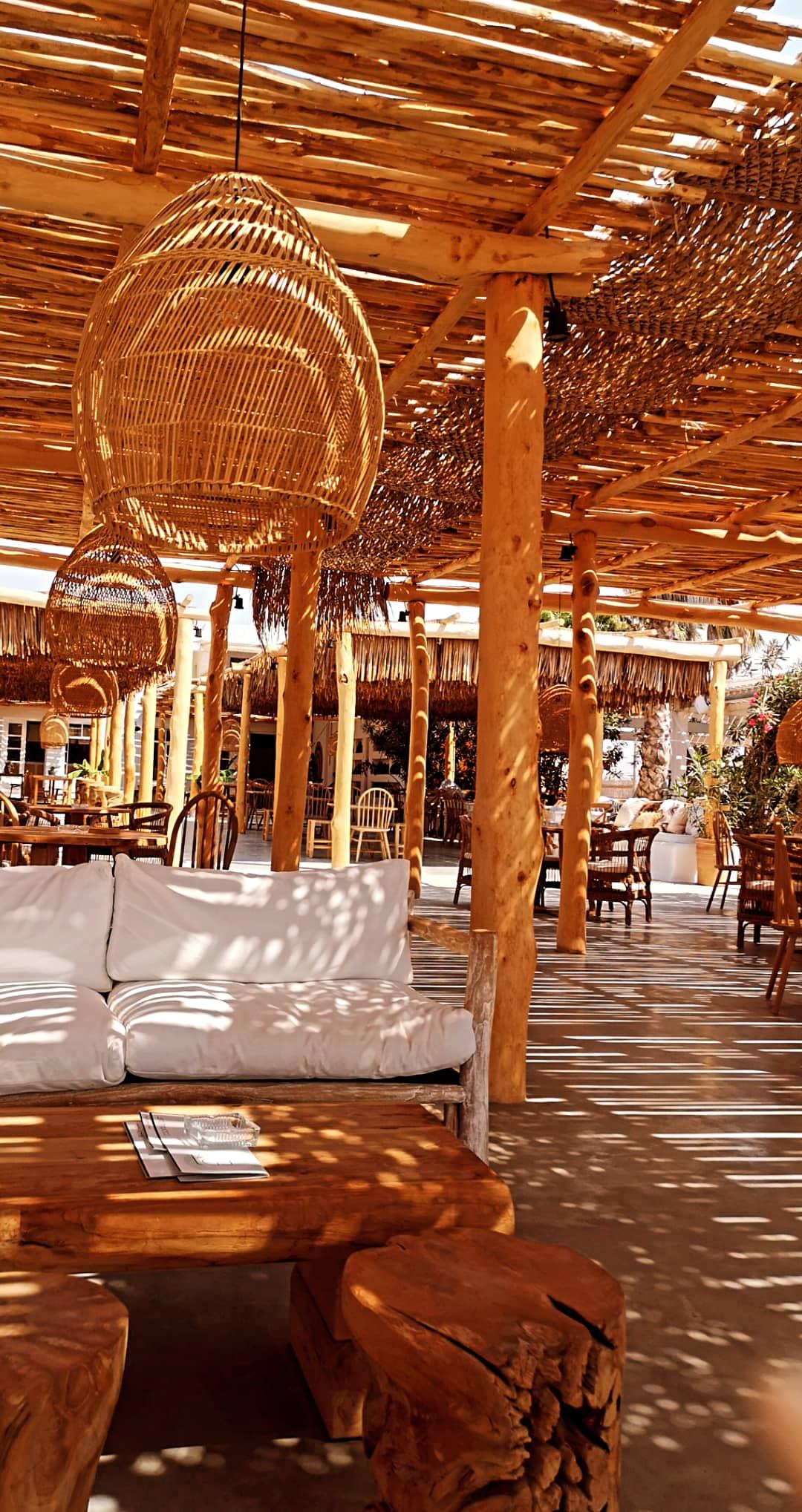 Wood and straw dining area and beachfront tables at Nomad on Plaka beach in Naxos
