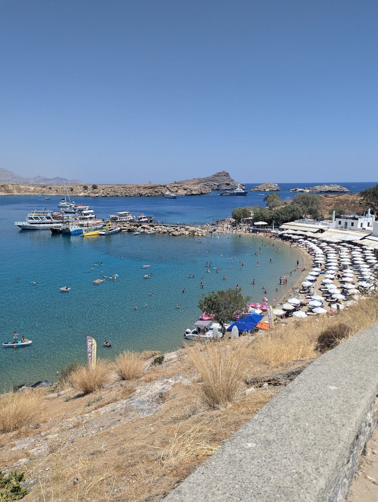 Sandy main bay of Pallas beach with shallow water and the Acropolis of Lindos rising on the headland above on the east coast of Rhodes