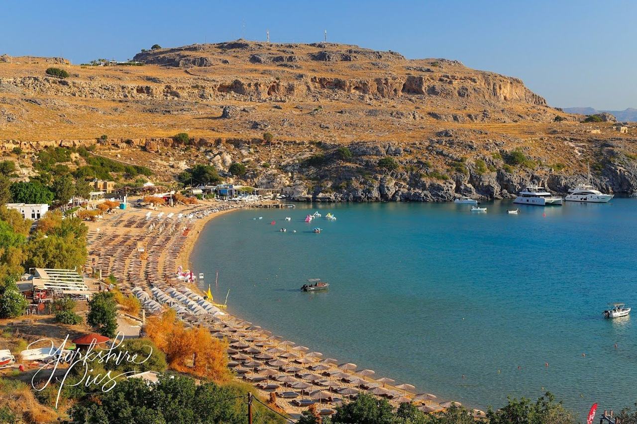 Looking down over the sandy bay of Pallas beach and its sunbeds with the whitewashed houses and Acropolis of Lindos above on Rhodes