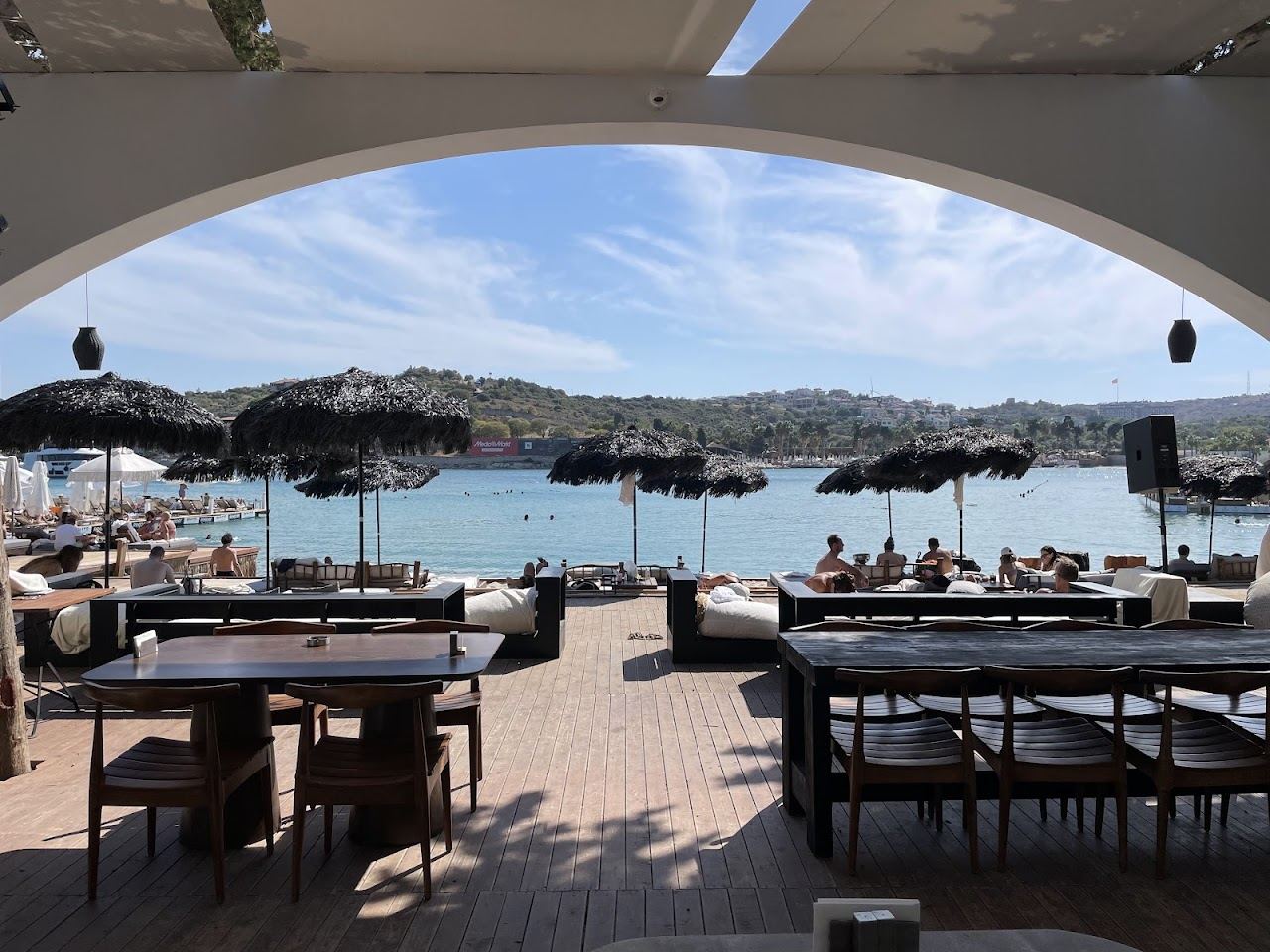 Sunbeds and umbrellas on the wooden sea deck of Paparazzi Beach Club above the water at Ayayorgi cove, Cesme