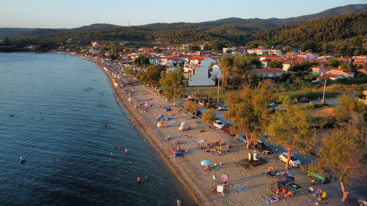 Sand and pebble shore with shallow clear water and tavernas behind at Paradisos beach in Neos Marmaras on Sithonia in Halkidiki