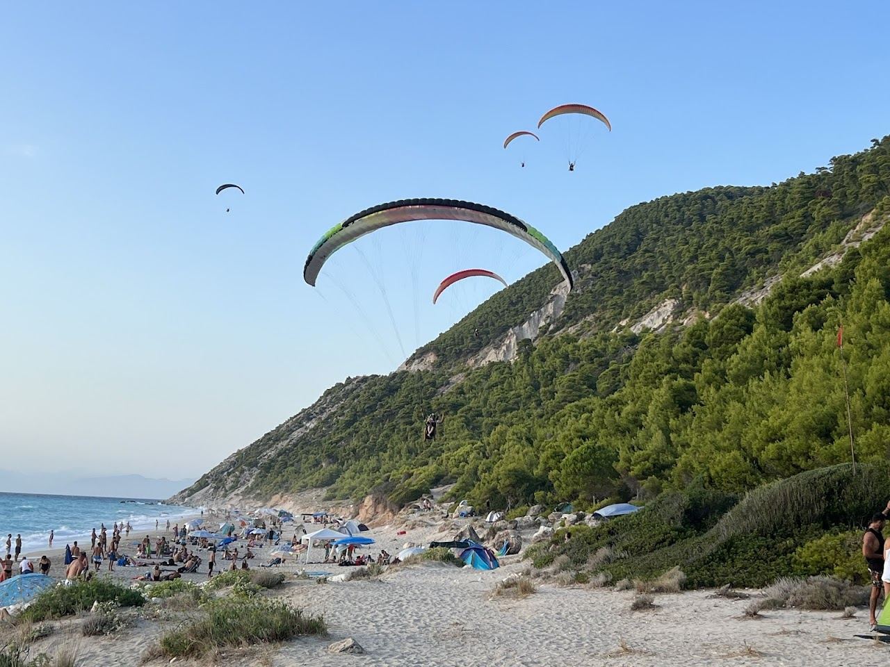 The long pale sand and gravel sweep of Pefkoulia beach with turquoise water below green hills north of Agios Nikitas on Lefkada