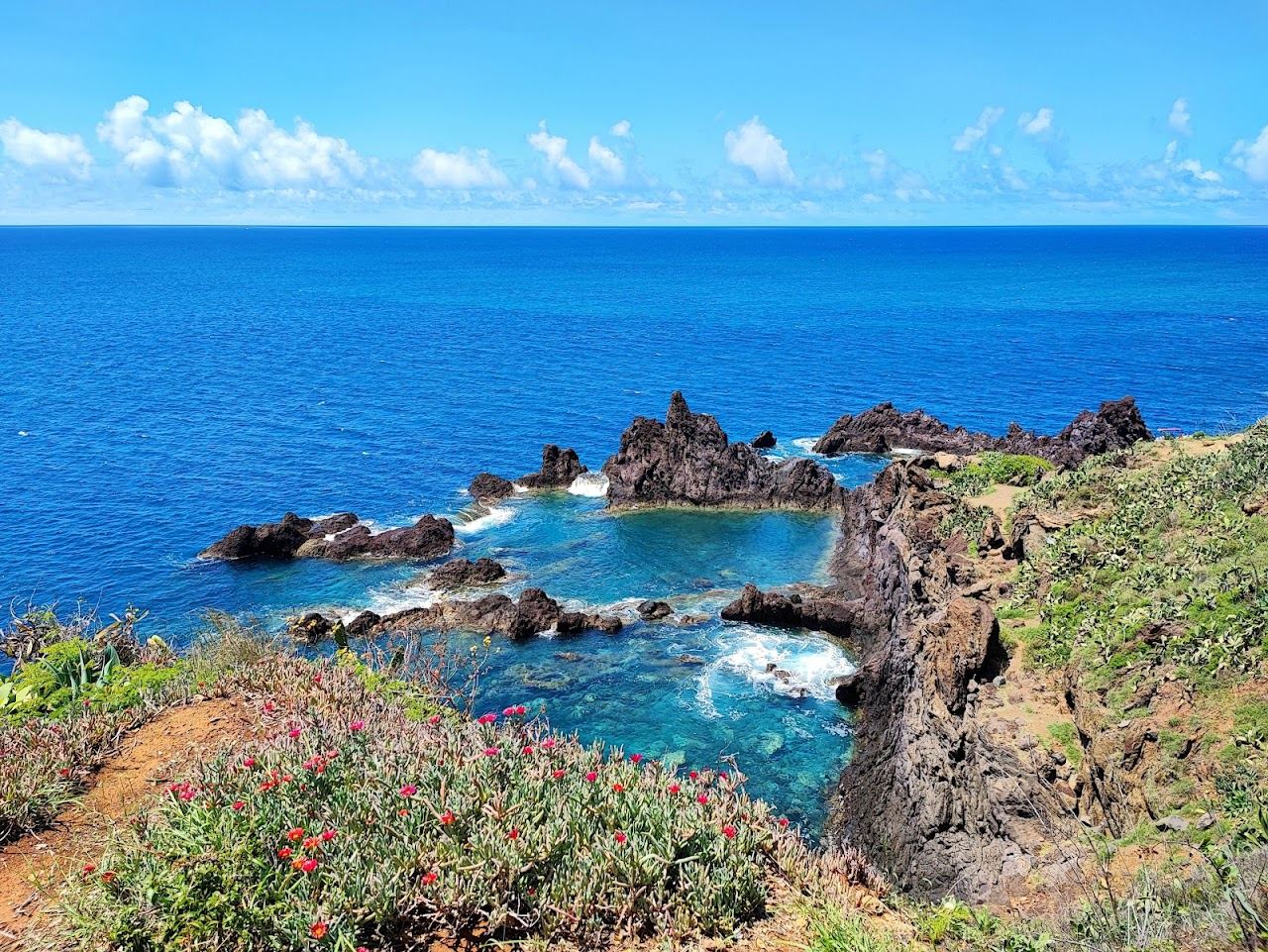 Bathers on the rock framed tidal pool and sea access at Ponta Gorda with the open Atlantic beyond