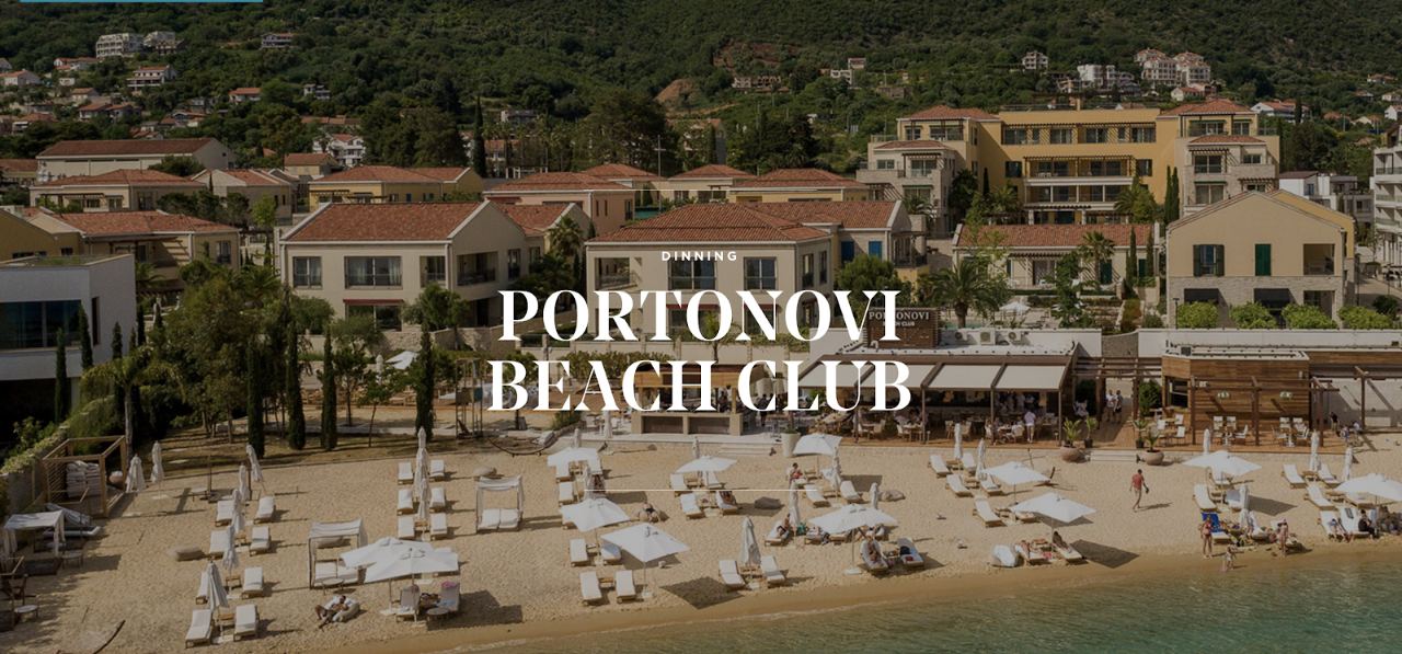 Sunbeds and umbrellas on the sandy shore of Portonovi Beach Club beside the calm water of Boka Bay