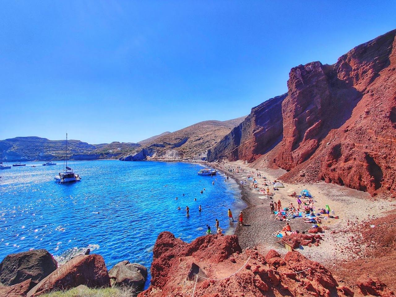 The rust red volcanic cliffs framing the cove of Red Beach near Akrotiri on Santorini