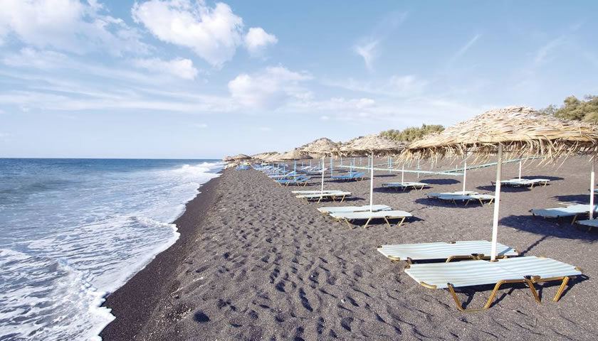 Long stretch of dark volcanic sand meeting clear water at Perissa Beach in southern Santorini