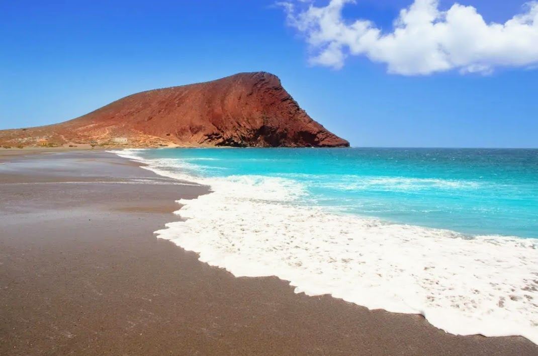 A wide golden beach below the Montana Roja cone at sunset on the south coast of Tenerife
