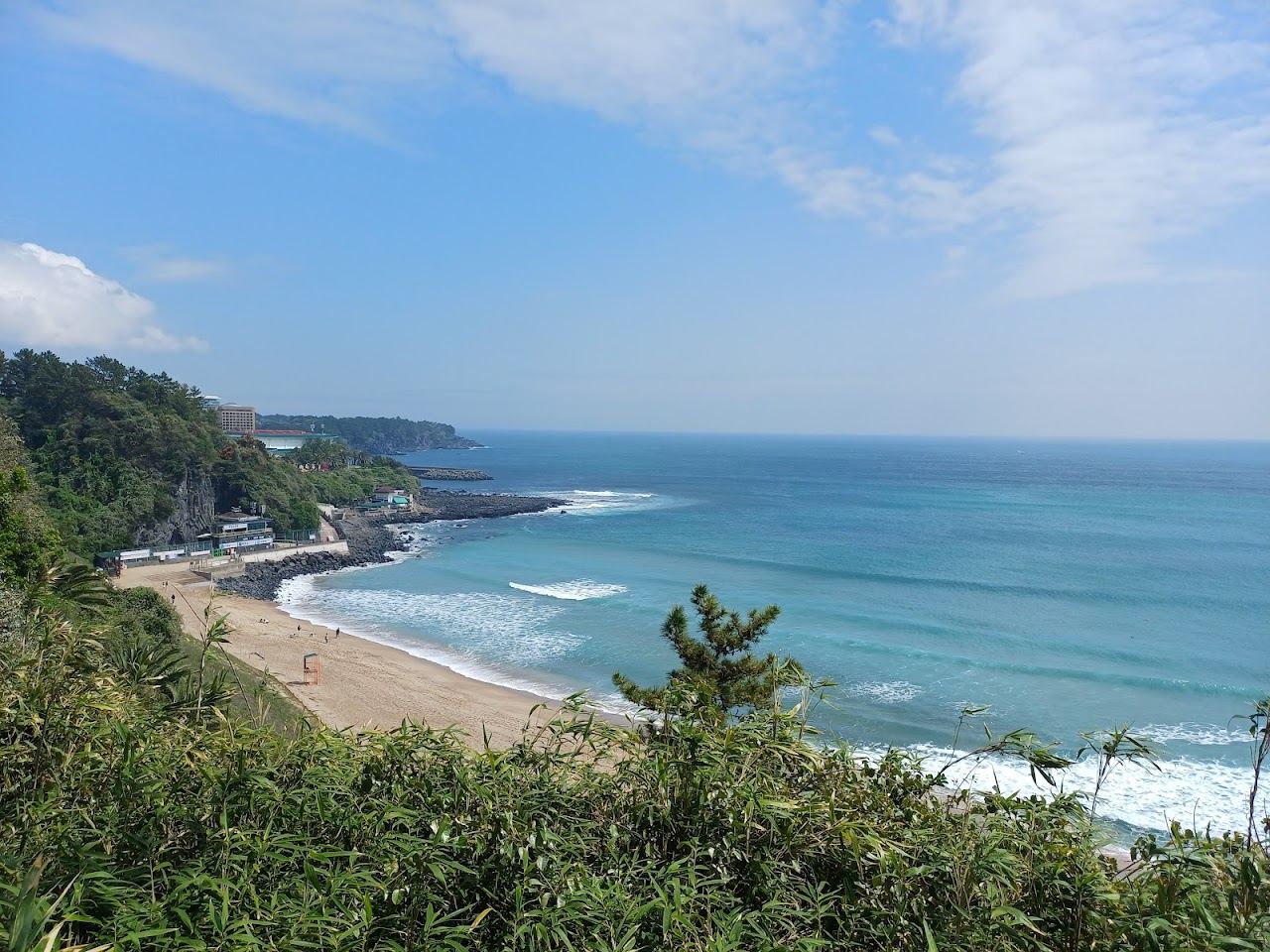Waves rolling onto the sand at Jungmun Saekdal beach beneath the cliffs of Jeju