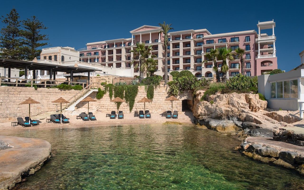 Sunbeds and white umbrellas on the rock platforms of The Reef Club lido at Dragonara Point, St Julian's