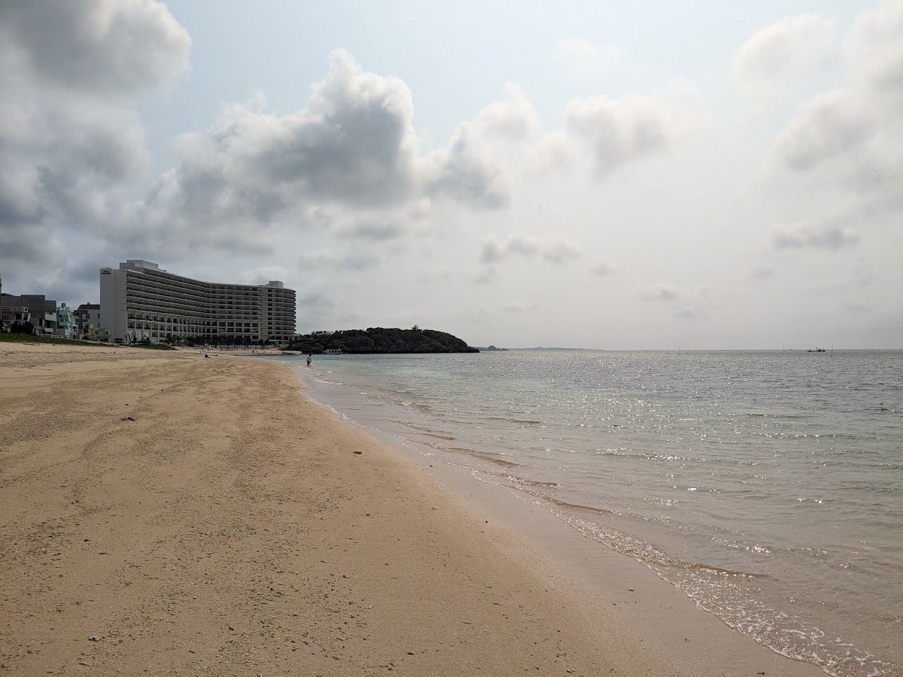 The curve of natural white sand at Fuchaku with clear shallows in front of the Onna resort strip