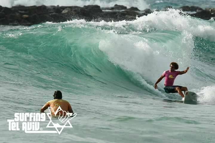 Two surfers on a green reef wave off Tel Aviv, one riding the open face while the other paddles over the shoulder
