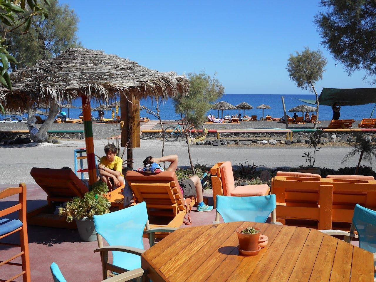 Colourful bohemian tables and shaded seating at Tranquilo beach bar on the black sand of Perissa in Santorini