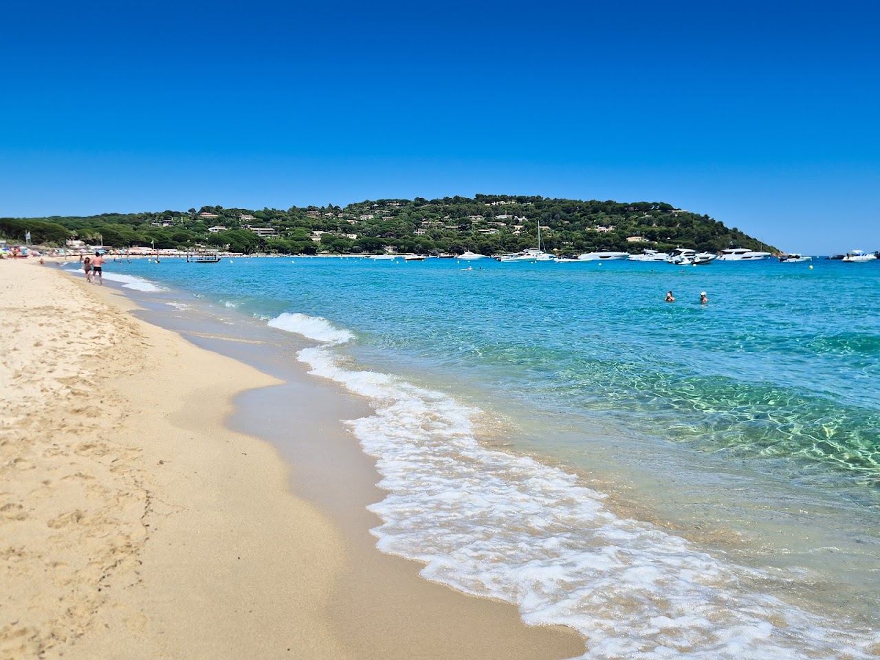 Pale sand and calm clear water along Pampelonne bay at Ramatuelle, looking down the open public beach