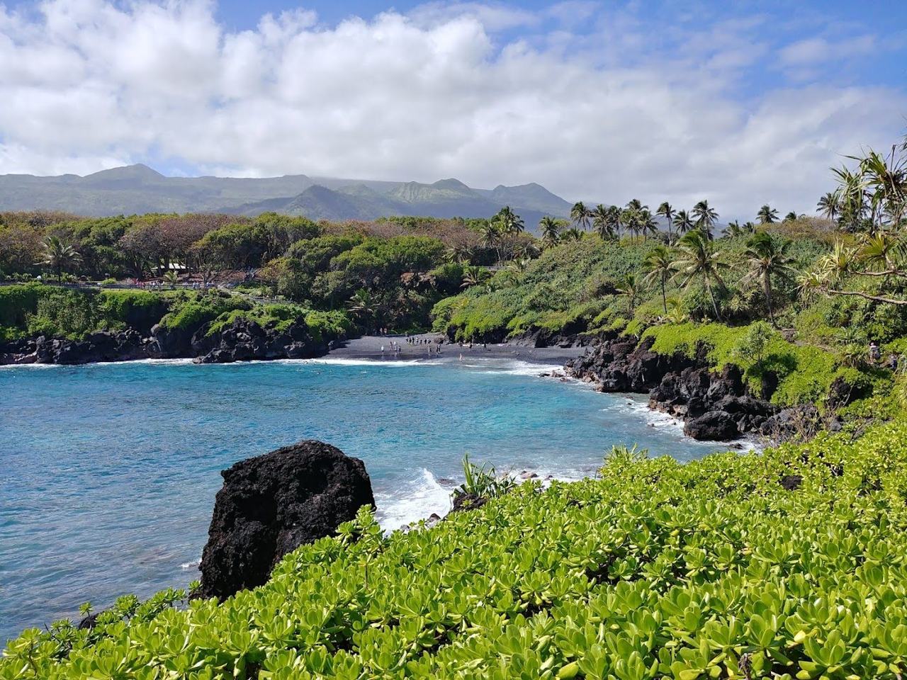 Waianapanapa black sand beach near Hana Maui a dark pebble cove framed by green lava cliffs and blue surf