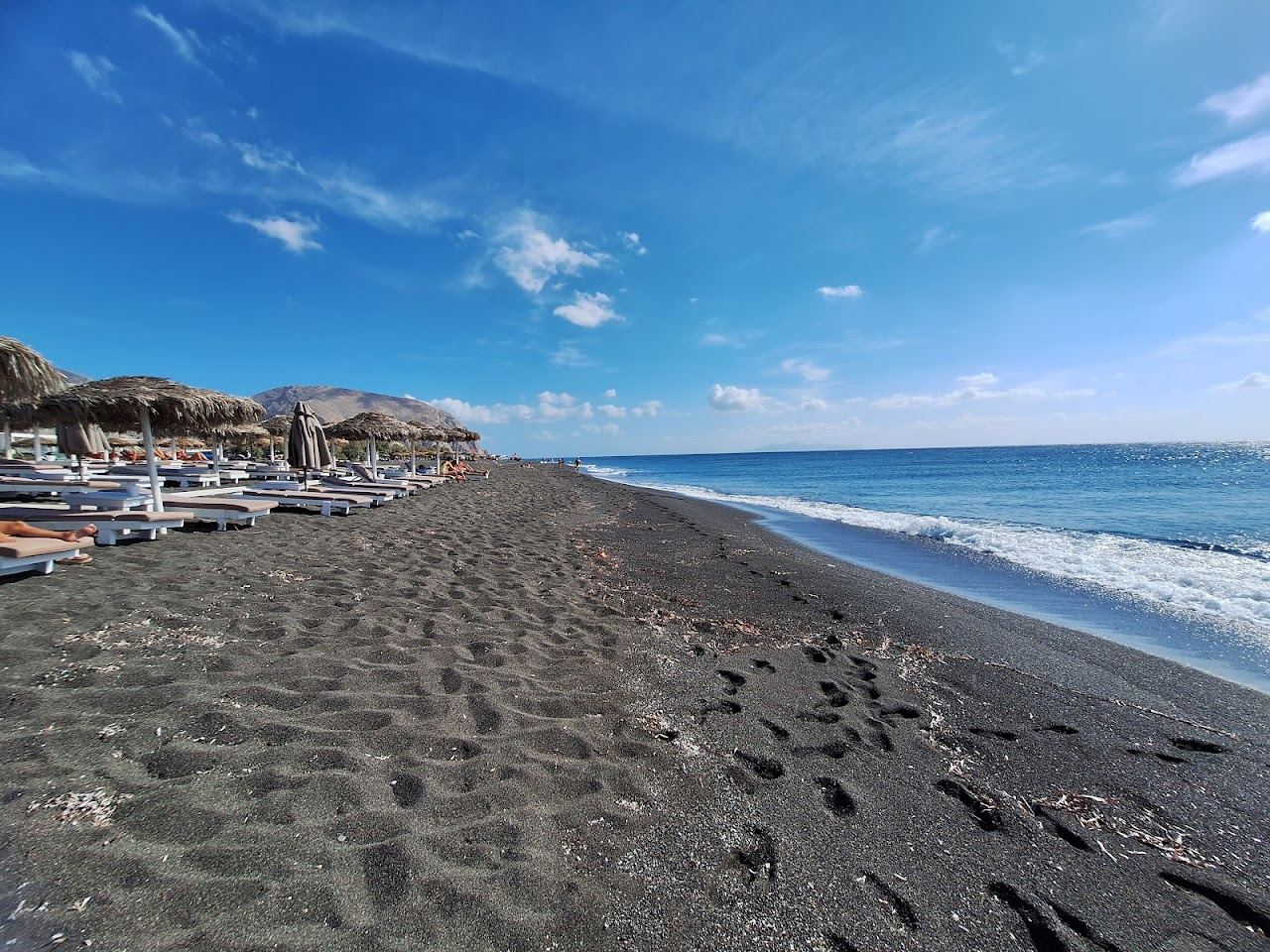 The long black volcanic sand of Perivolos beach stretching along the southeast coast of Santorini